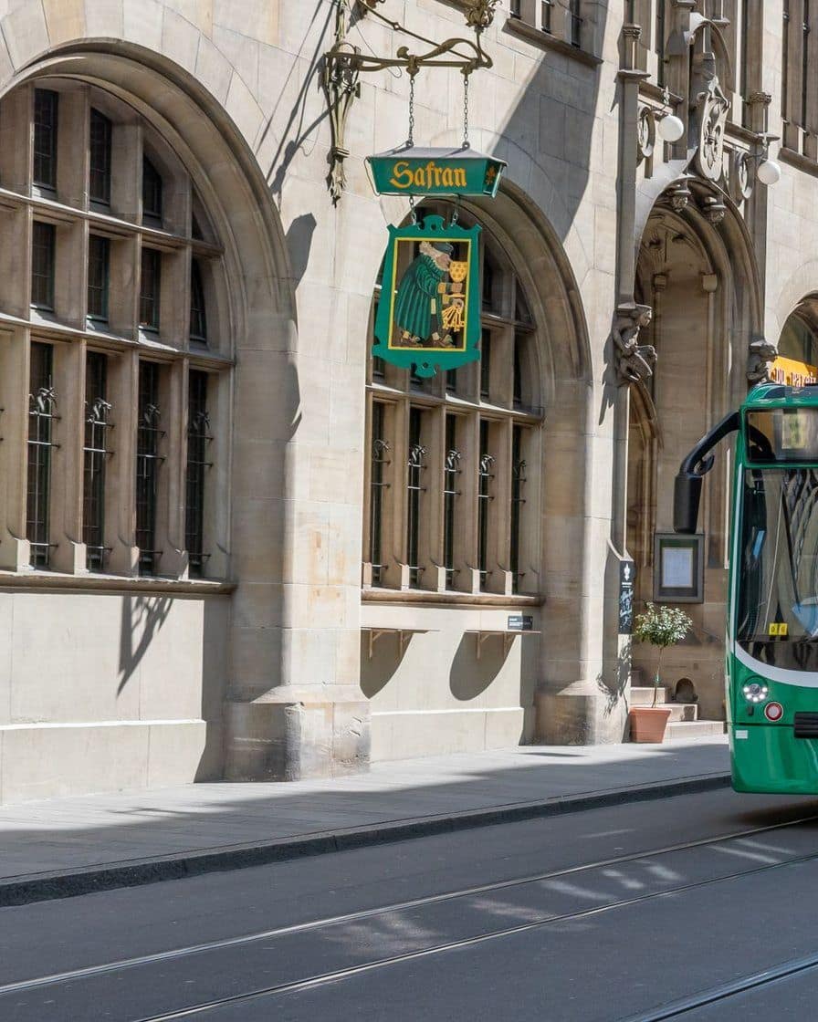 A green Basel tram in front of a sandstone building with Gothic windows