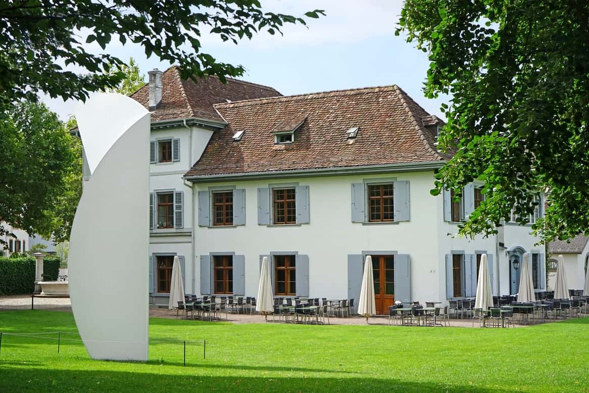 Die weisse Villa Berower im Park der Fondation Beyeler in Riehen, davor eine grosse helle Skulptur auf dem Rasen