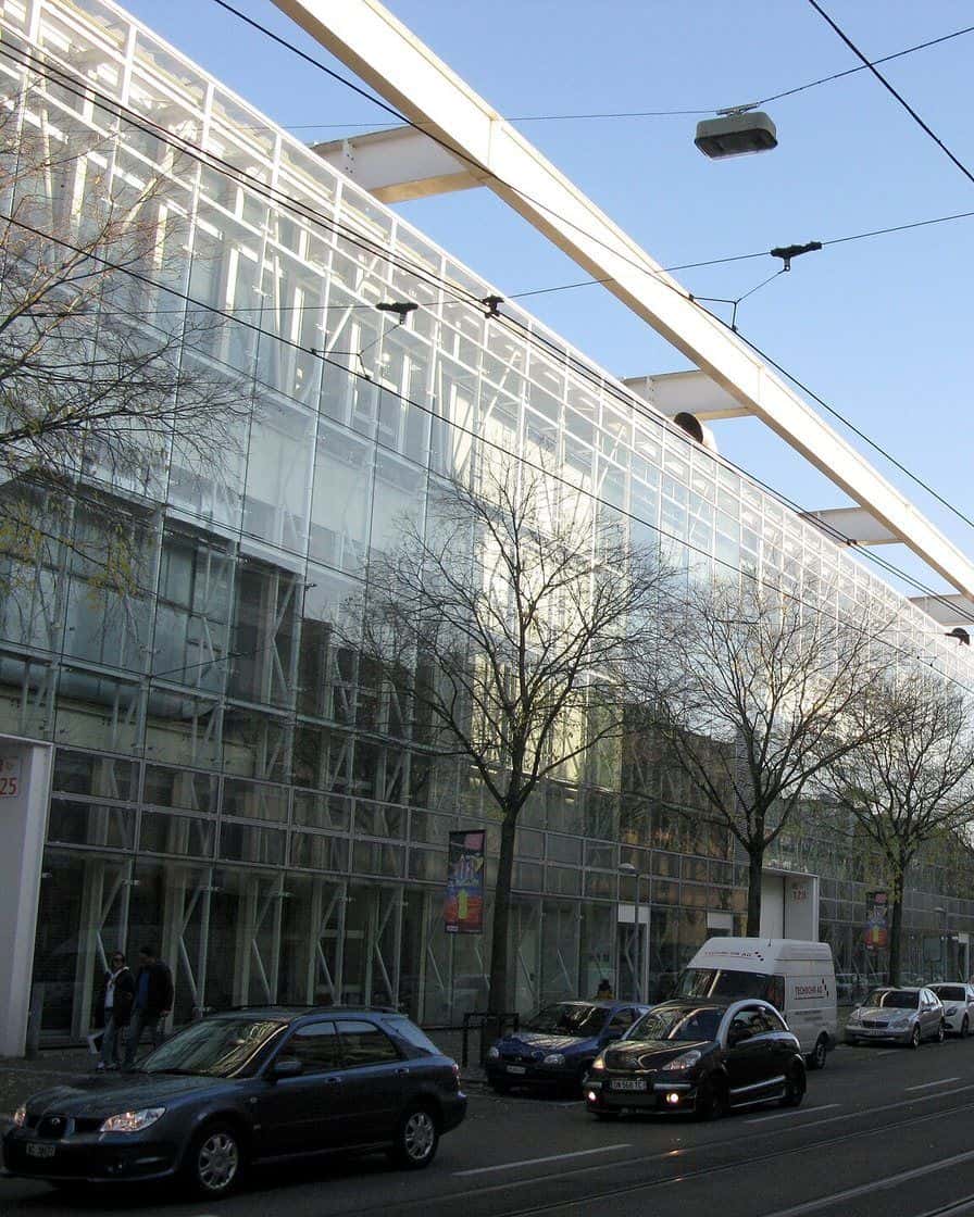 La halle 1 de la Messe Basel avec sa façade de bandes métalliques signée Herzog et de Meuron au-dessus de la Messeplatz, avec des visiteurs devant
