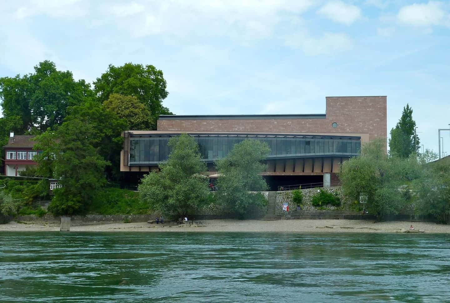 Das Museum Tinguely von Mario Botta im Solitude-Park, vom Rhein aus gesehen, mit Bäumen am Ufer