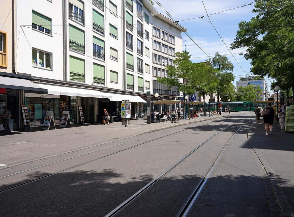 Die Untere Rebgasse in Kleinbasel mit Geschäften, Tramgleisen und Bäumen an einem sonnigen Tag