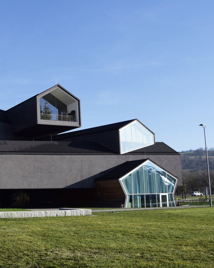 Das VitraHaus von Herzog & de Meuron in Weil am Rhein, gestapelte dunkle Hausvolumen mit Satteldächern und grossen Glasgiebeln, davor eine Wiese